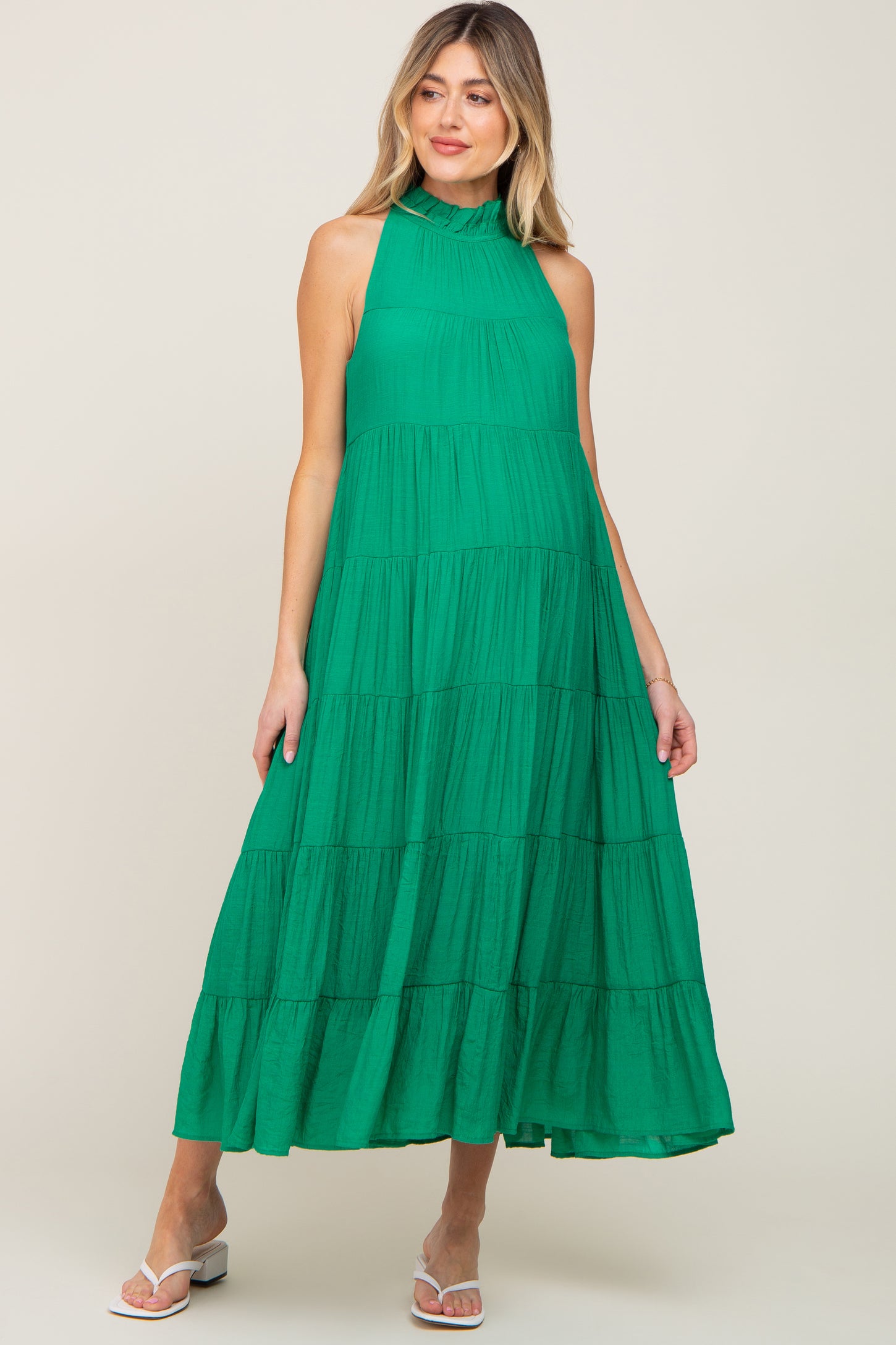 woman wearing a green tiered halter maternity maxi dress with a ruffled neckline and white sandals