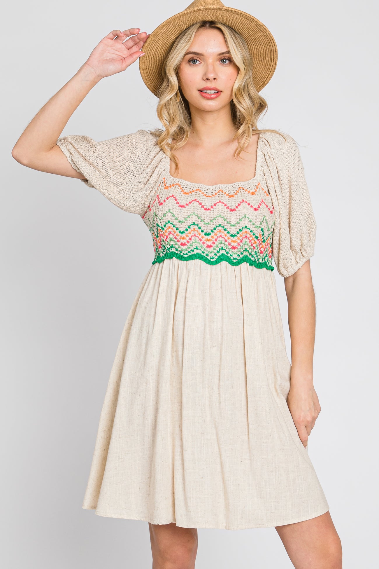 woman wearing a beige puff sleeve dress with colorful crochet bodice and a straw hat