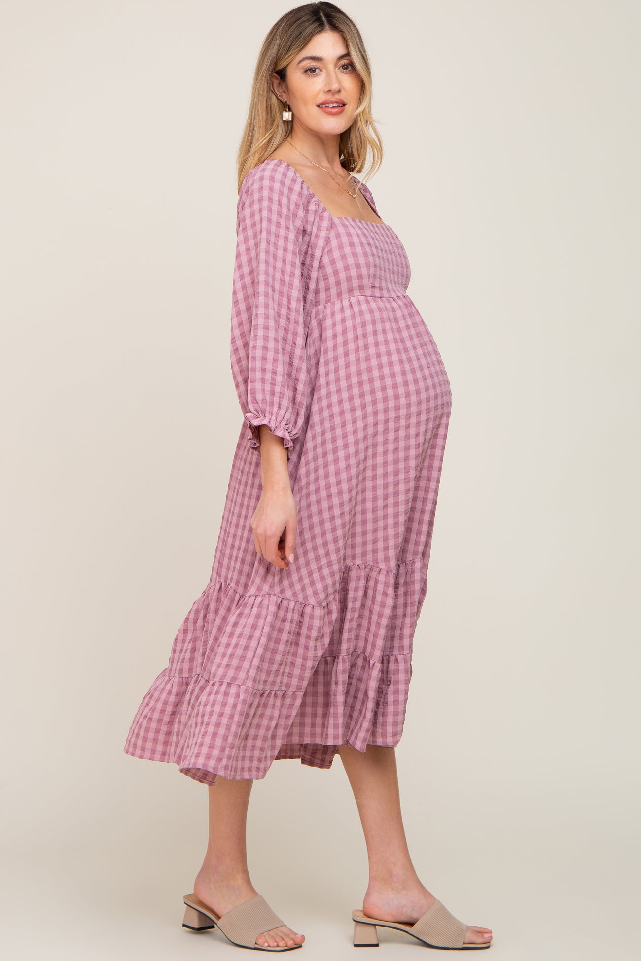 Pregnant woman wearing a pink gingham maternity midi dress with long sleeves and tiered skirt