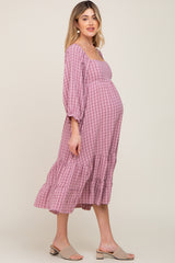 Pregnant woman wearing a pink gingham maternity midi dress with long sleeves and tiered skirt