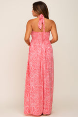 Back view of a woman wearing a pink floral halter maxi dress with a smocked bodice and tie neck.