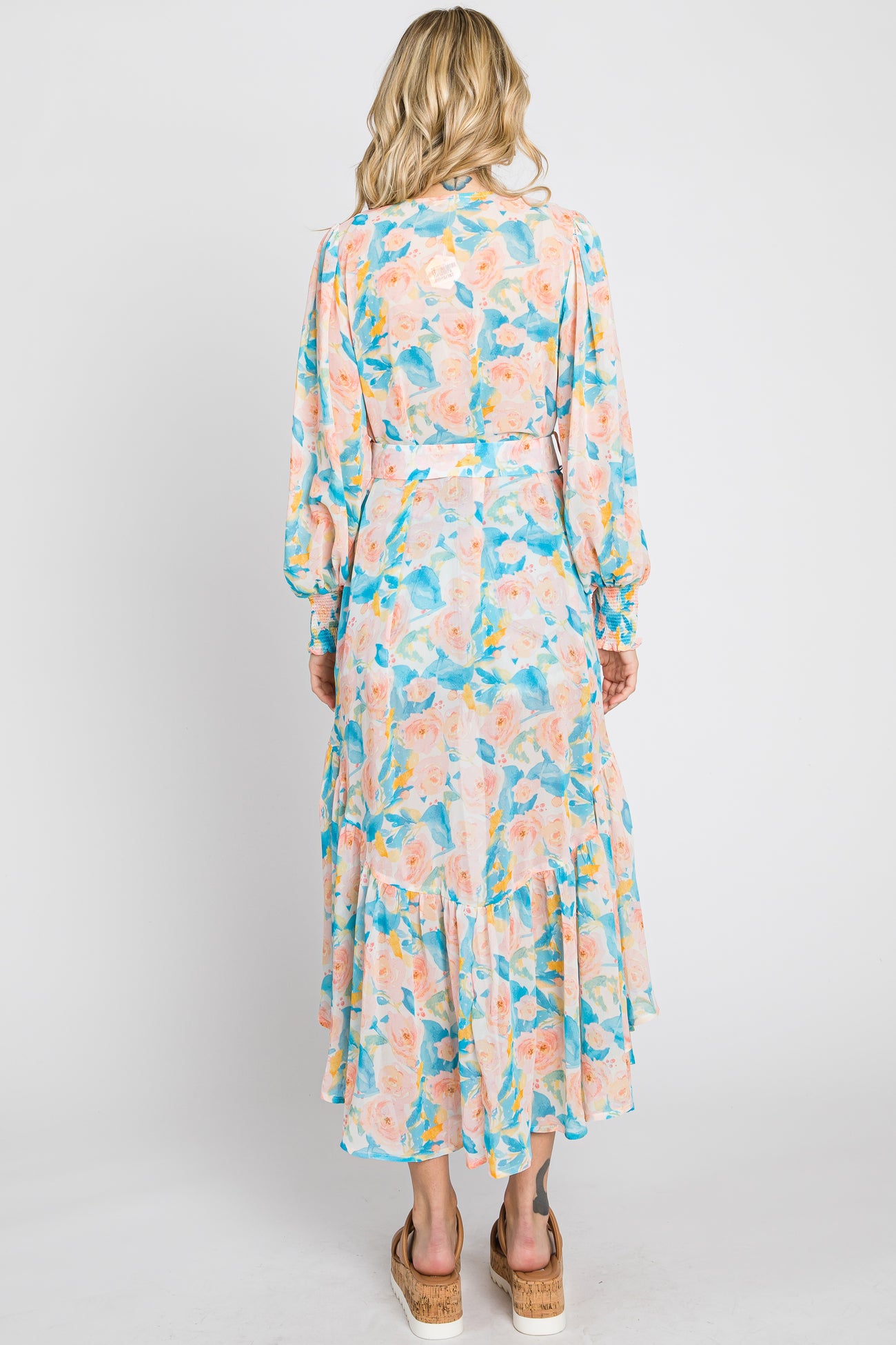 Back view of a woman wearing a long sleeve floral maxi dress with a belted waist and ruffled hem