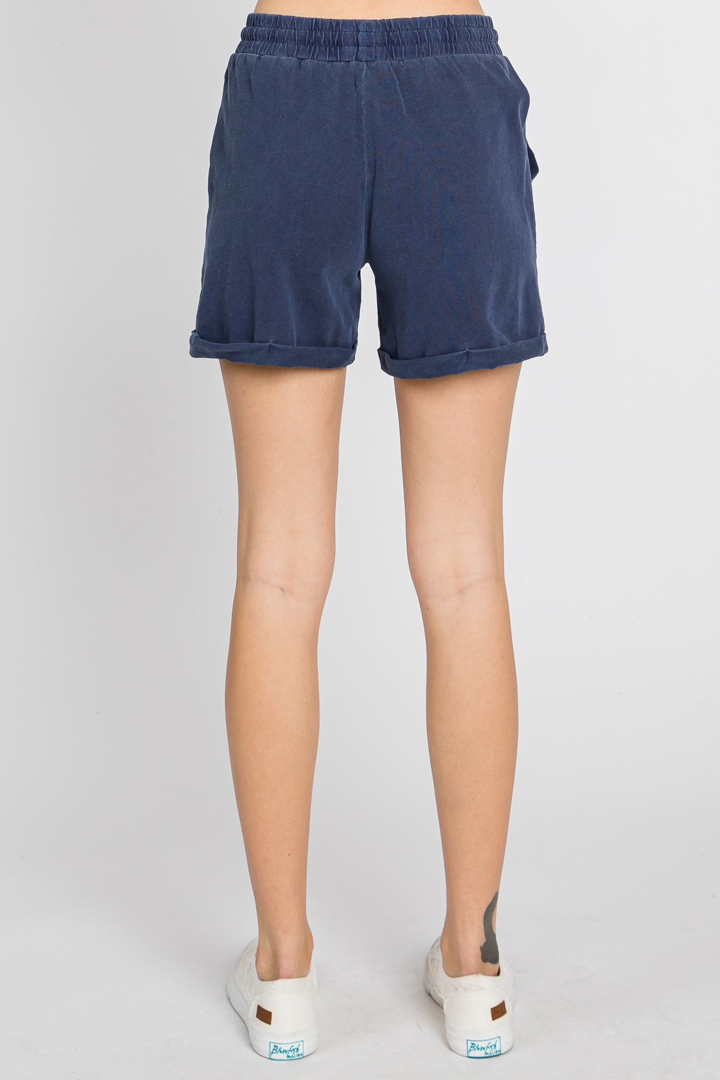 back view of a person wearing navy blue elastic waist shorts with rolled hems and white sneakers