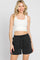 woman wearing a white ribbed crop tank top and black drawstring shorts against a white background