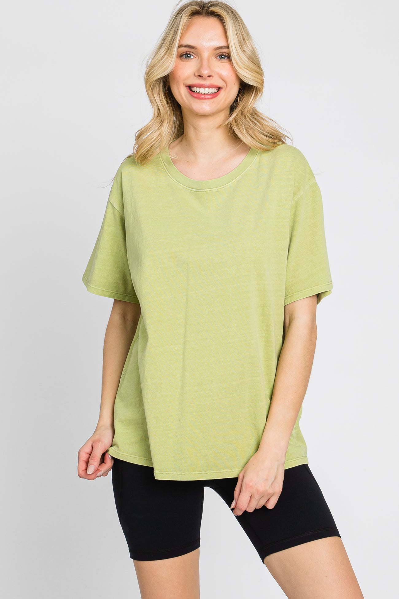 woman wearing an oversized lime green t-shirt and black biker shorts against a white background