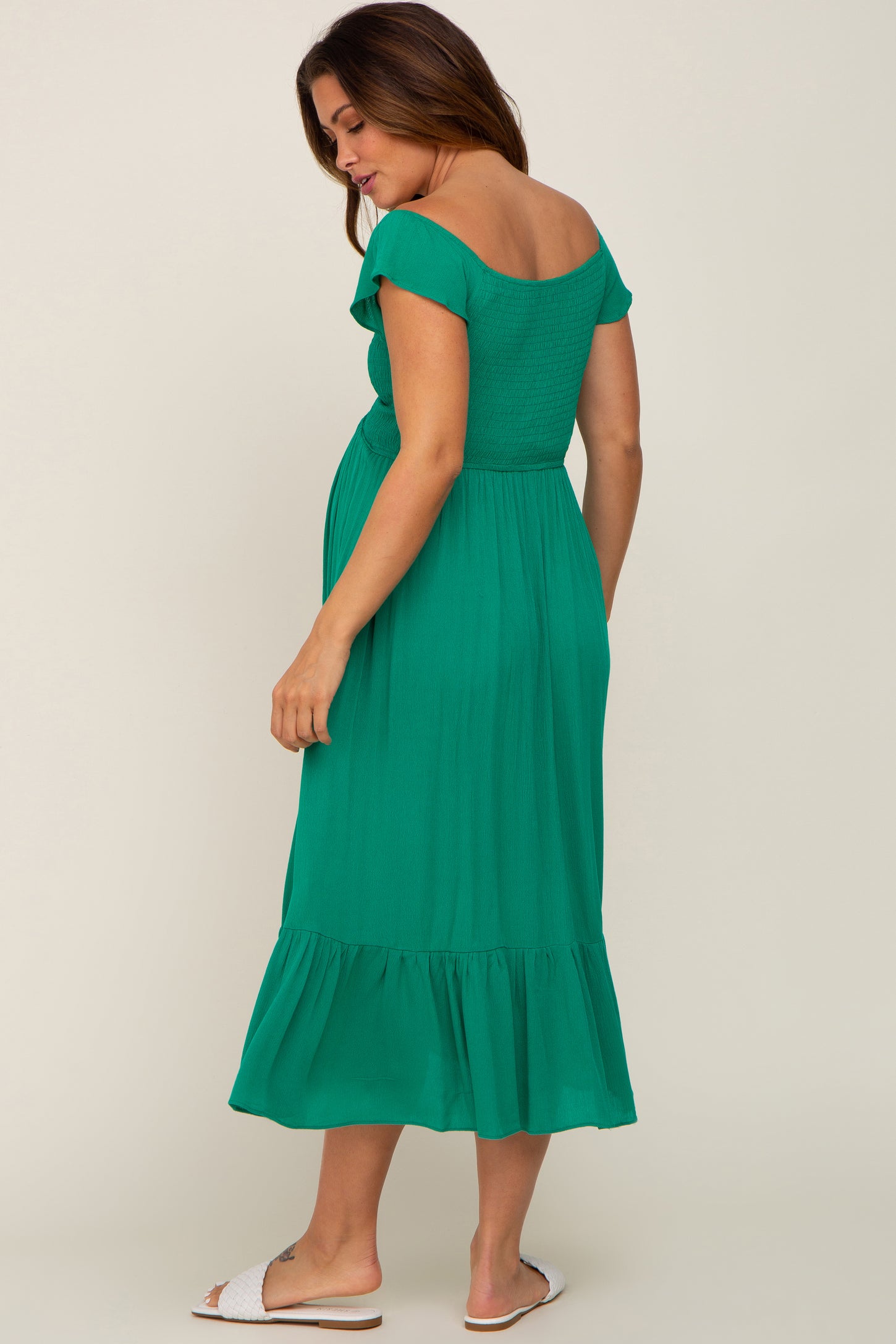 Pregnant woman wearing a green off-the-shoulder smocked maternity midi dress with ruffle hem