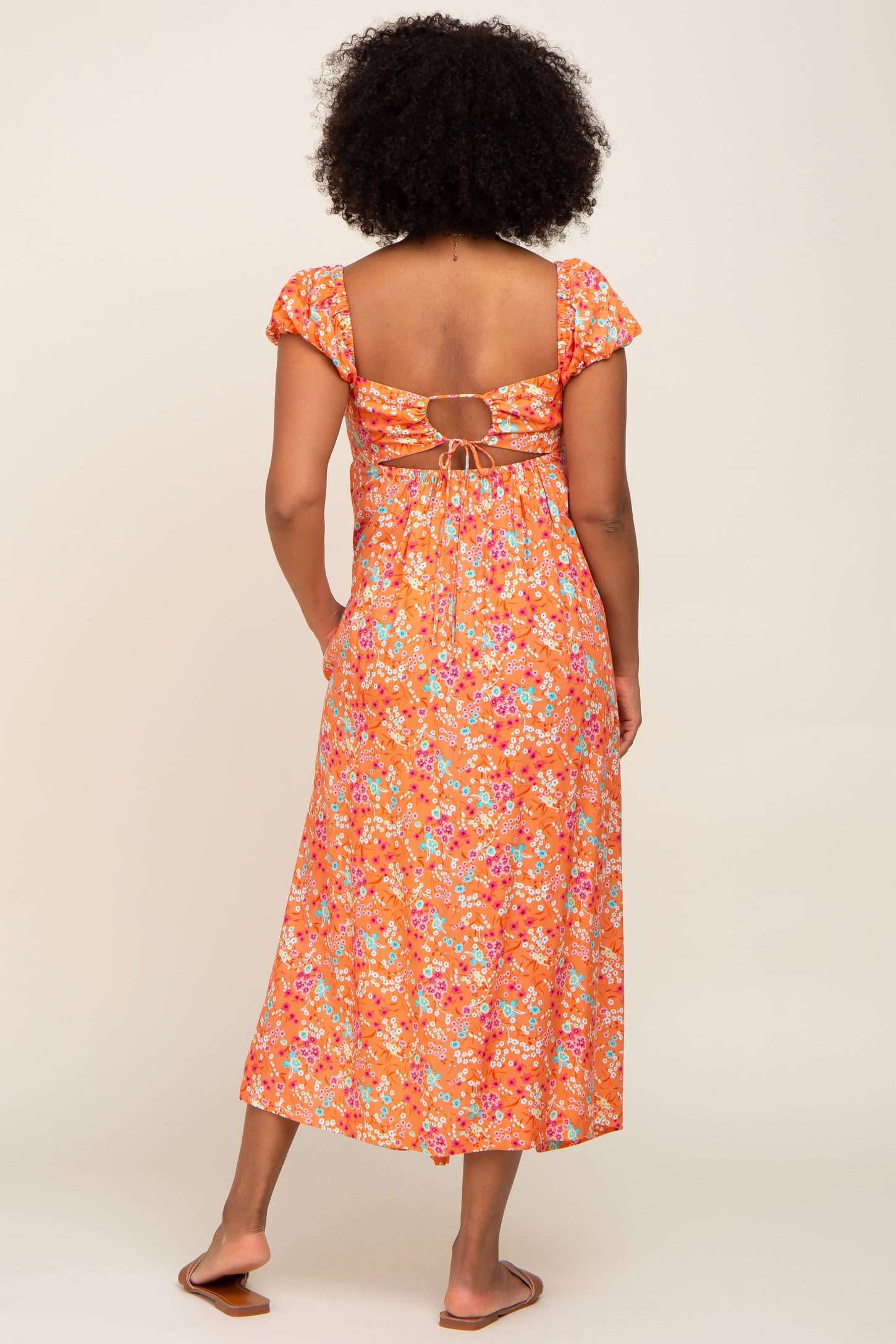 Back view of woman wearing orange floral midi dress with cutout back and puff sleeves
