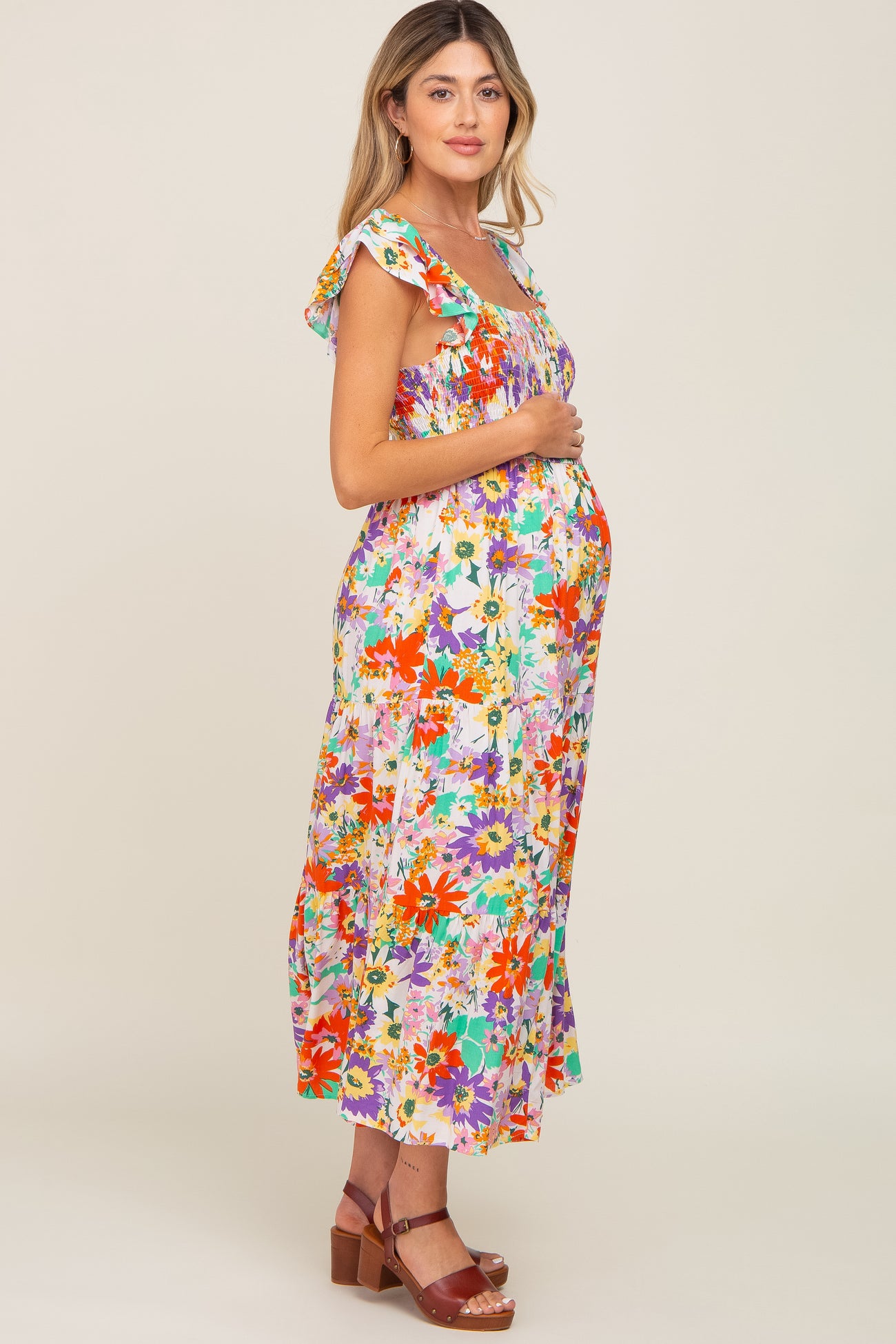 Pregnant woman wearing a colorful floral smocked maternity midi dress with ruffle sleeves and brown sandals