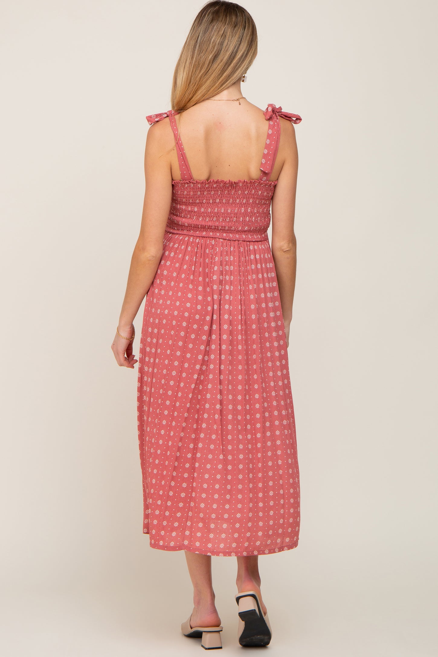 Back view of a woman wearing a mauve floral smocked midi dress with tie straps and a square neckline