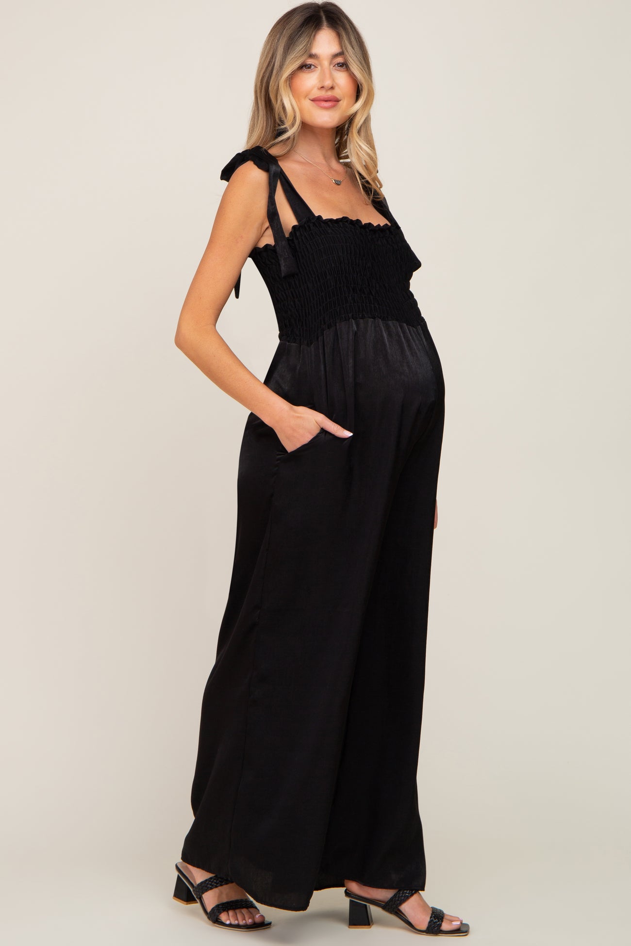 Pregnant woman wearing a black smocked maternity jumpsuit with tie straps and wide legs