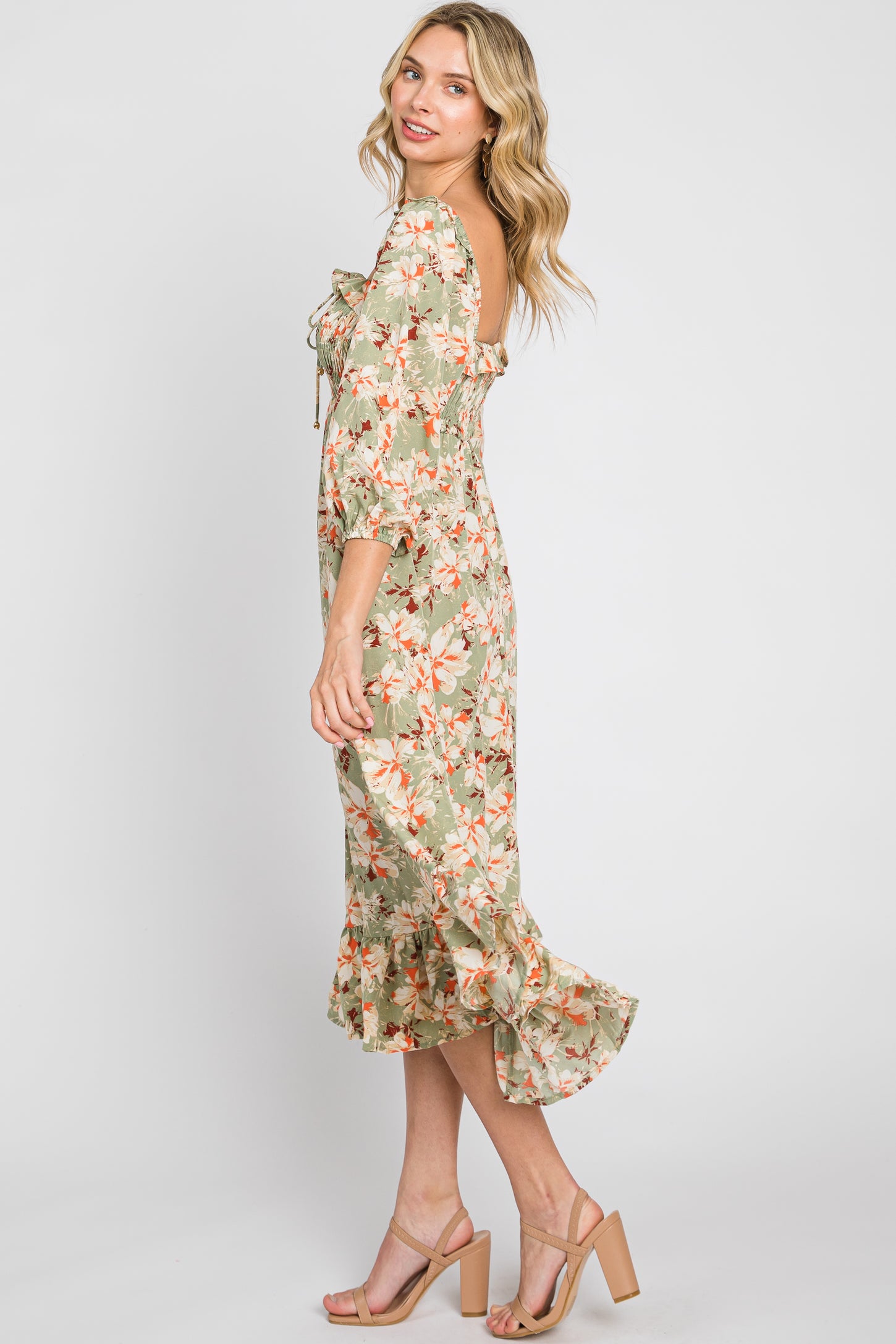 woman wearing a green floral midi dress with puff sleeves and a ruffled hem, standing sideways with a smile