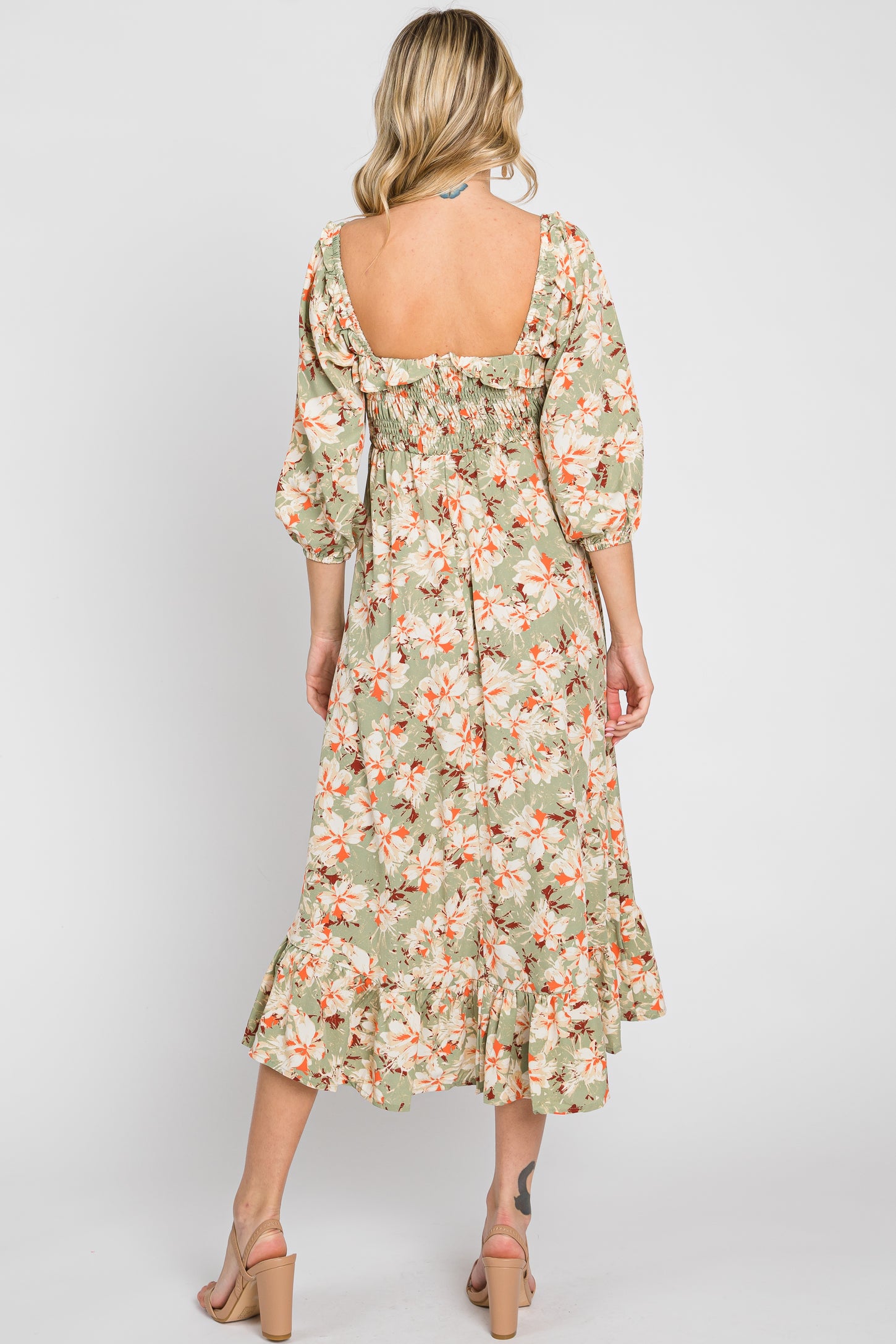 woman wearing a green floral midi dress with puff sleeves and a ruffled hem, showing a bare back