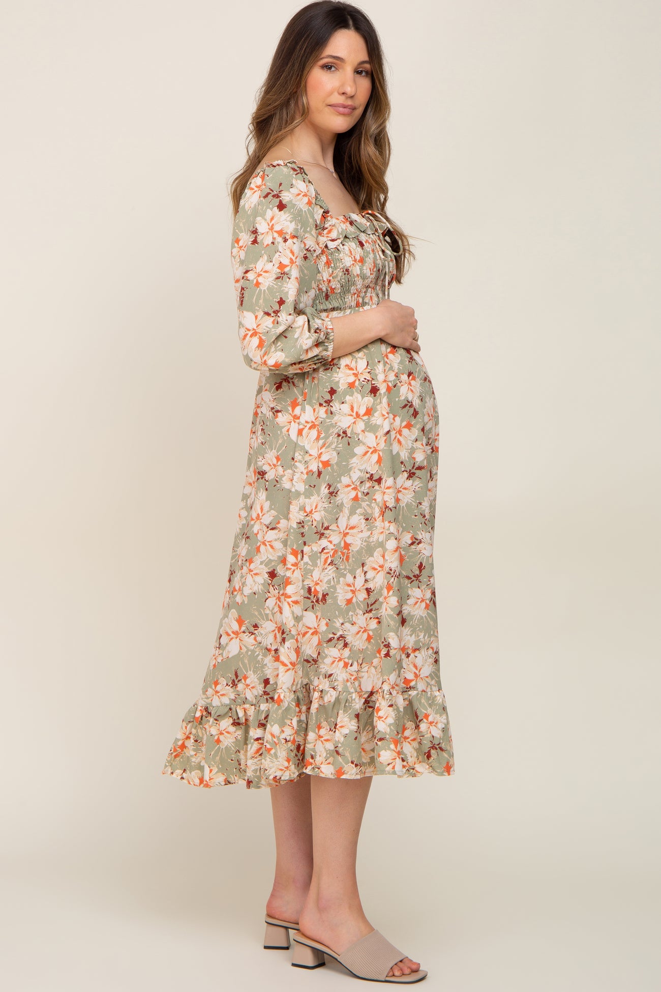 woman wearing a floral green maternity dress with a smocked bodice and ruffle hem, holding her baby bump