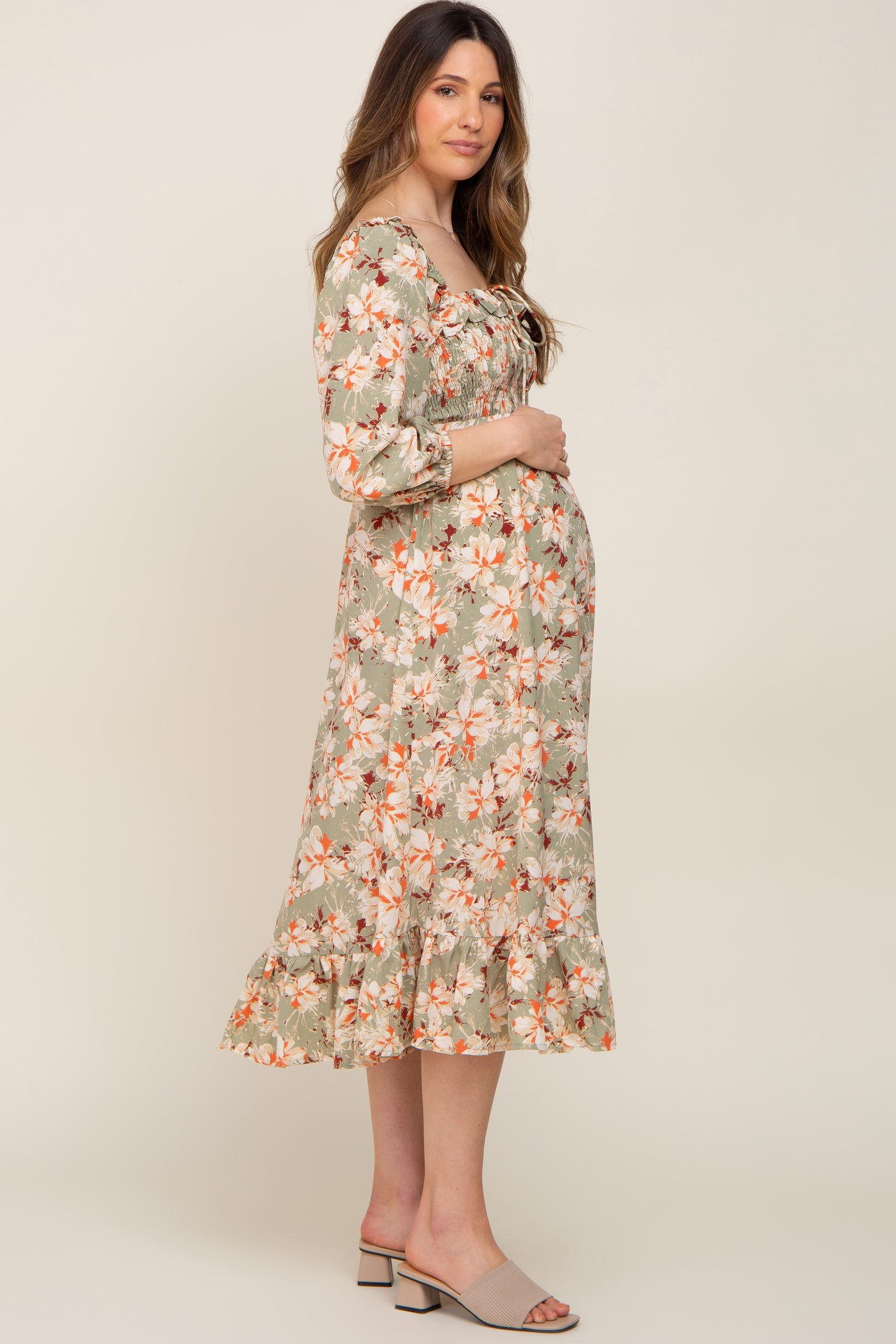 woman wearing a floral green maternity dress with a smocked bodice and ruffle hem, holding her baby bump