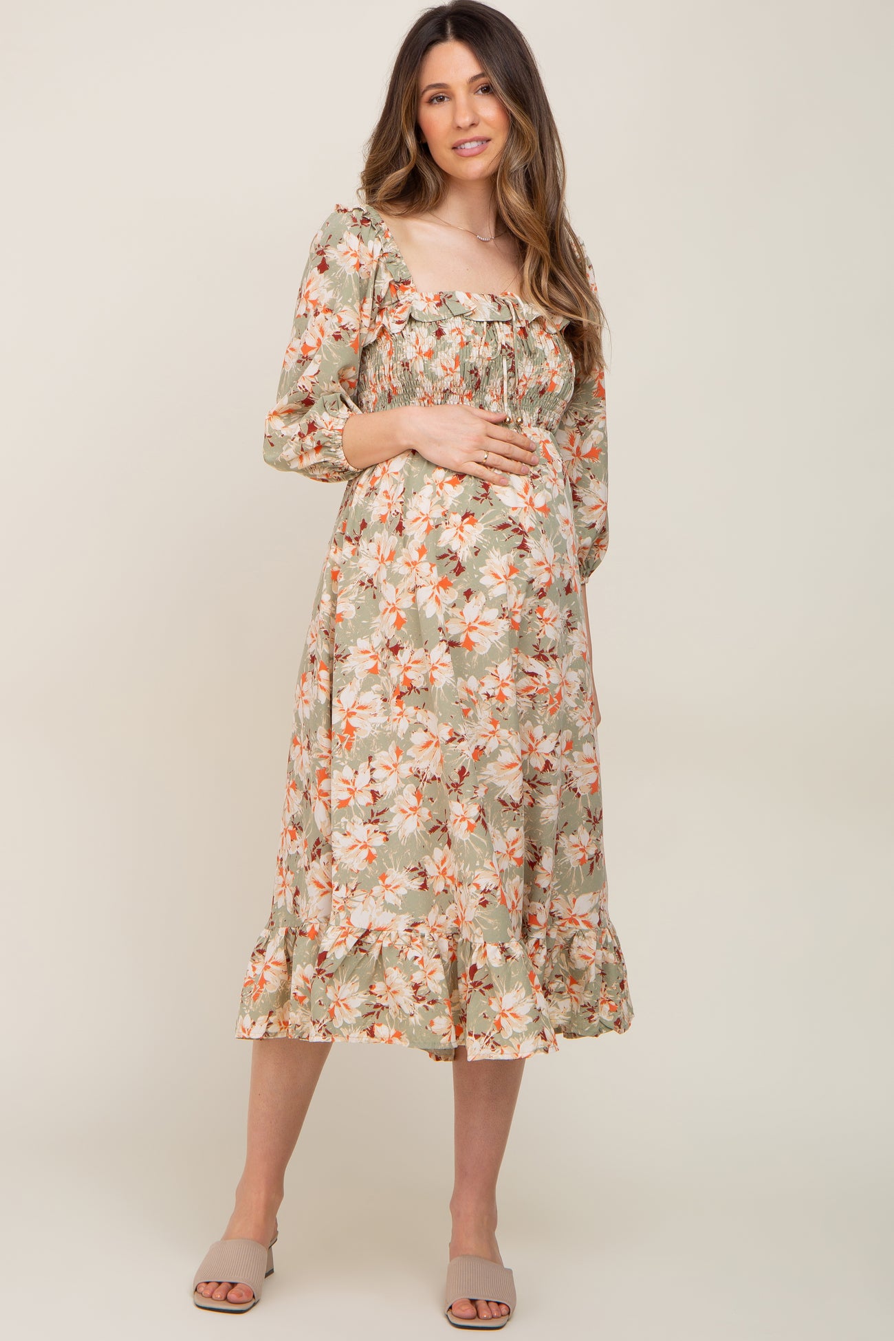 woman wearing a floral print maternity dress with three-quarter sleeves and a ruffled hem, holding her baby bump