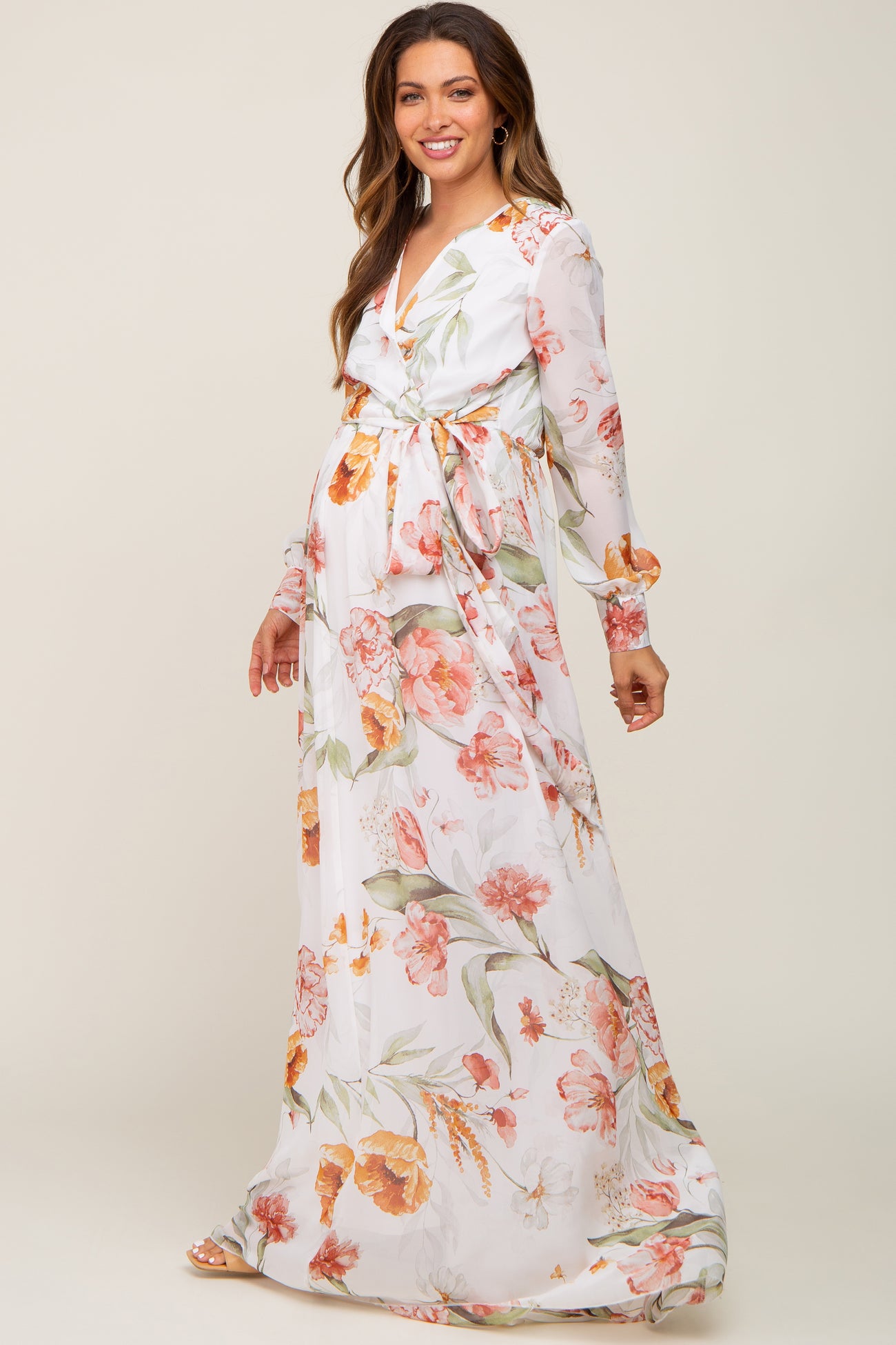 Pregnant woman wearing a white long sleeve floral maternity maxi dress with a waist tie
