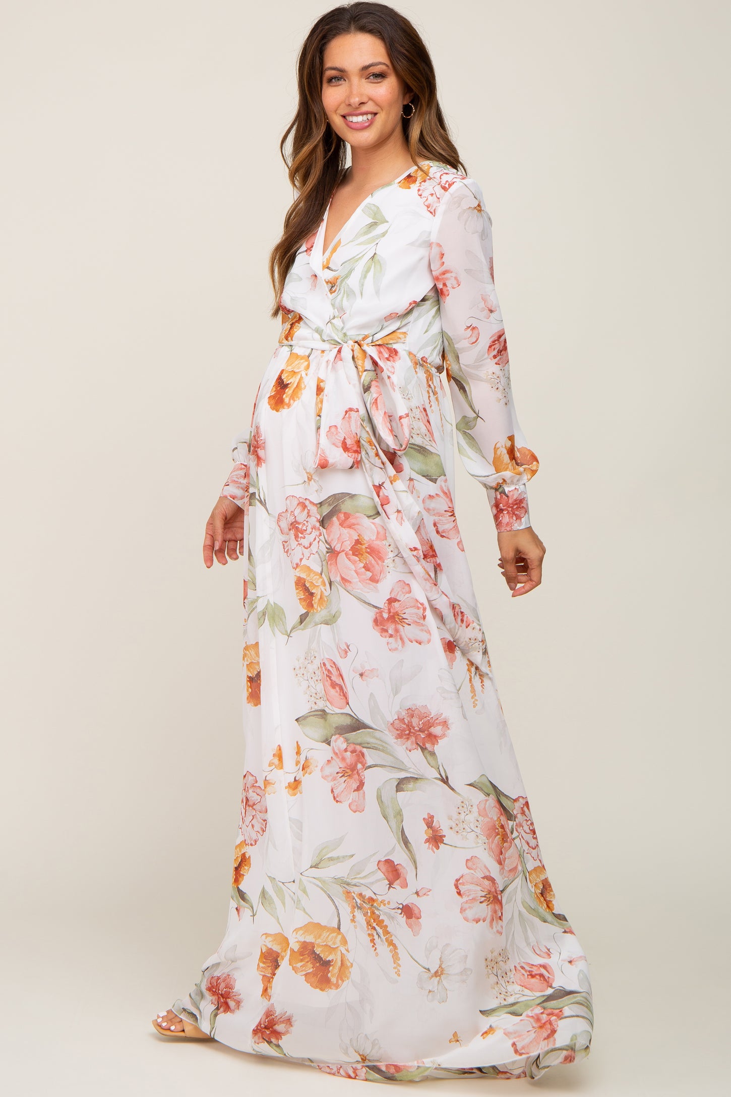 Pregnant woman wearing a white long sleeve floral maternity maxi dress with a waist tie