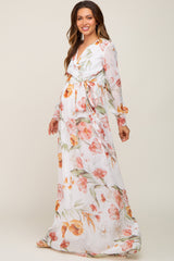 Pregnant woman wearing a white long sleeve floral maternity maxi dress with a waist tie