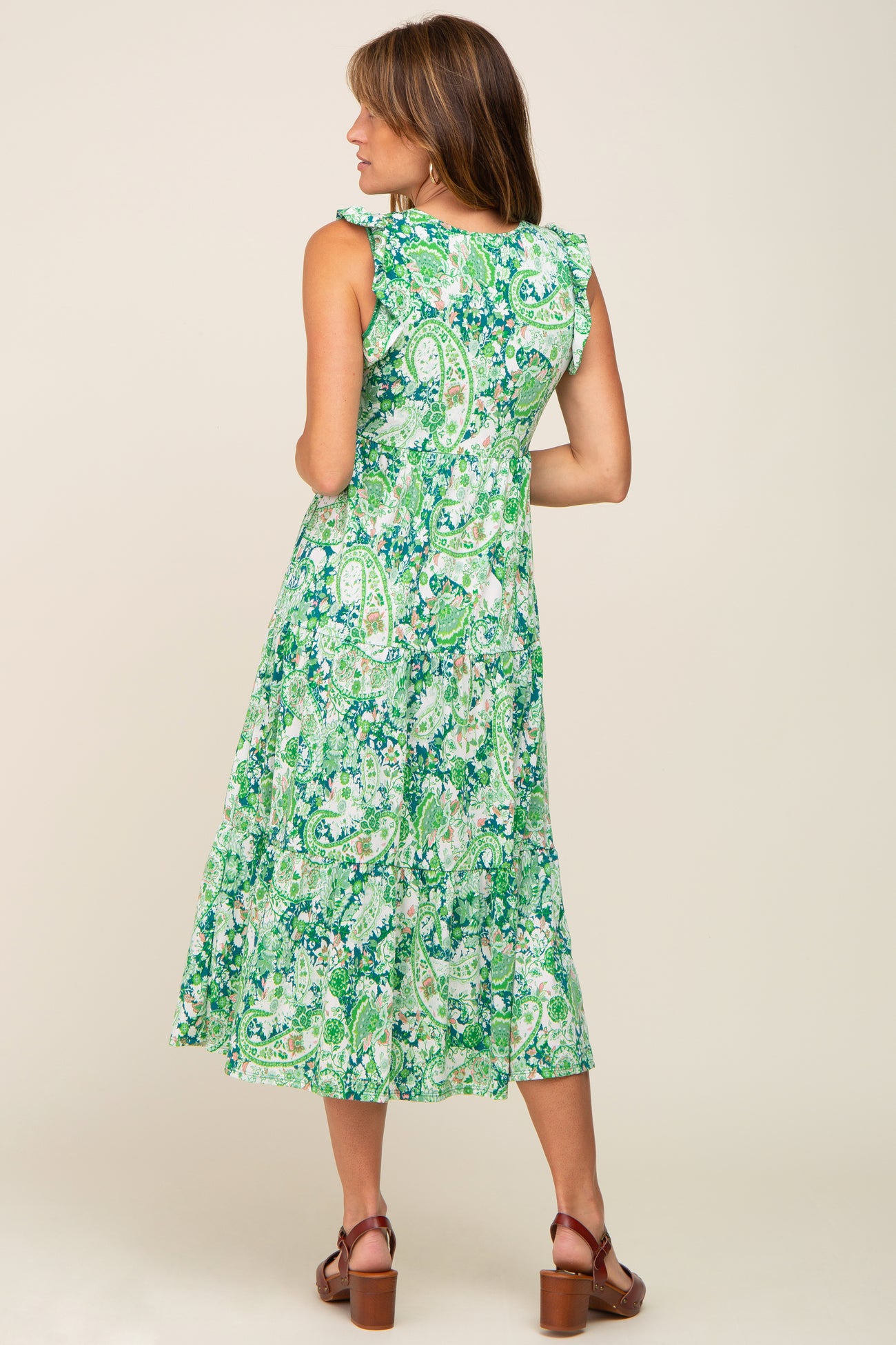 Woman wearing a green and white paisley print tiered midi dress with ruffle sleeves and brown clogs