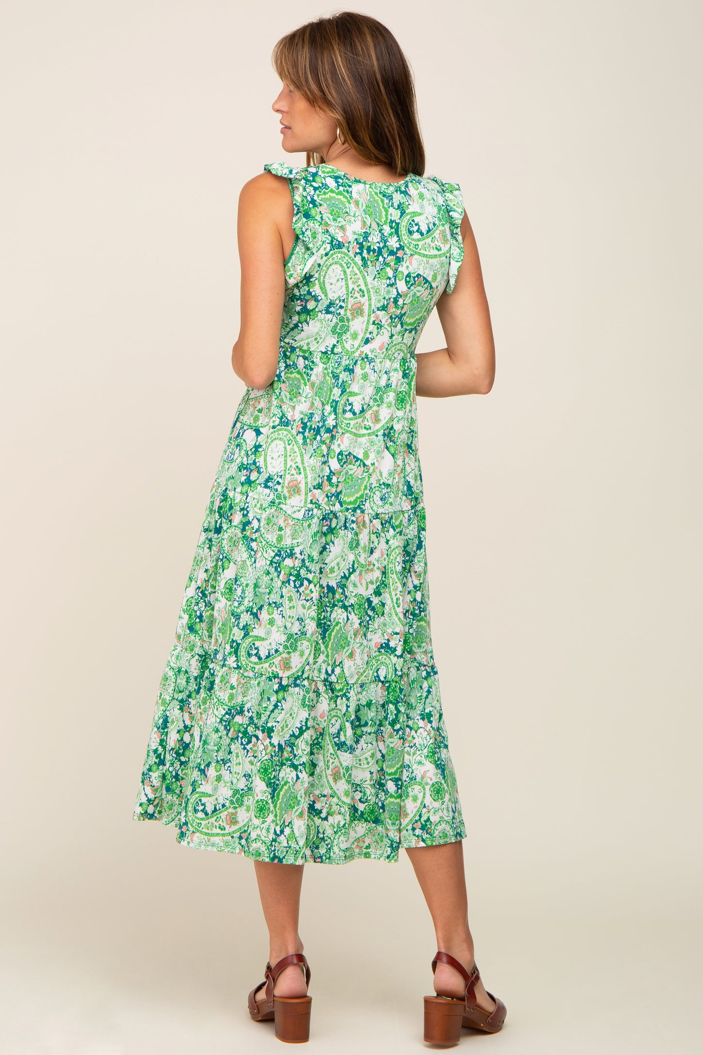 Woman wearing a green and white paisley print tiered midi dress with ruffle sleeves and brown clogs