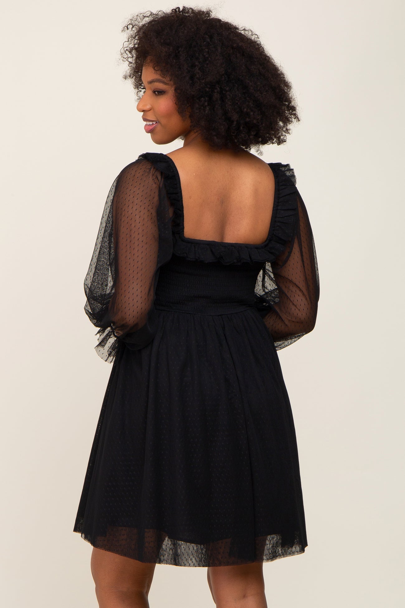 Woman wearing a black mesh puff sleeve dress with a square neckline and ruffle trim back view
