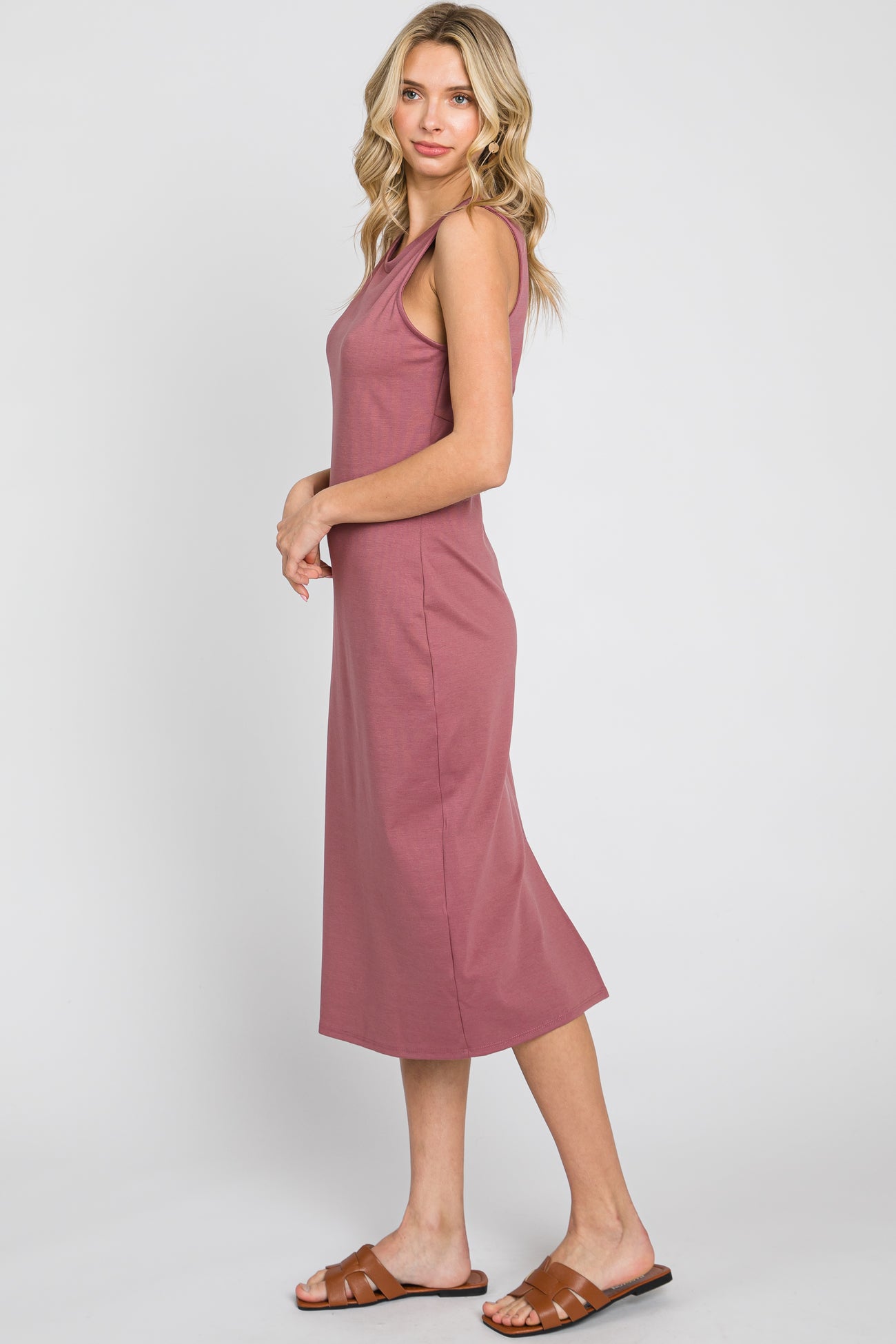 Woman wearing a mauve sleeveless midi dress and brown leather sandals against a white background