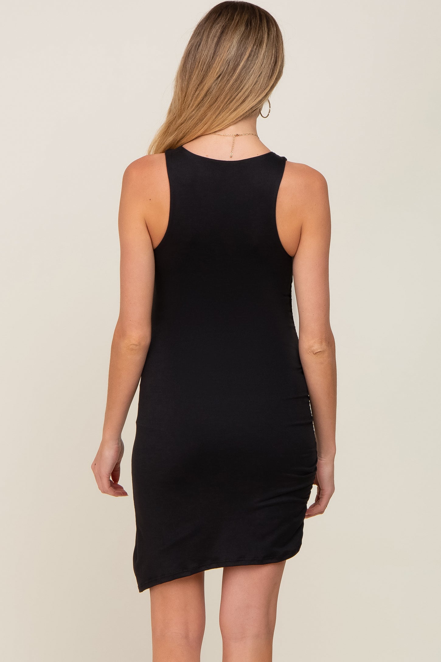 back view of a woman wearing a sleeveless black bodycon dress with an asymmetrical hemline