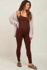 Pregnant woman wearing a brown ribbed maternity jumpsuit and beige cardigan with olive green sandals