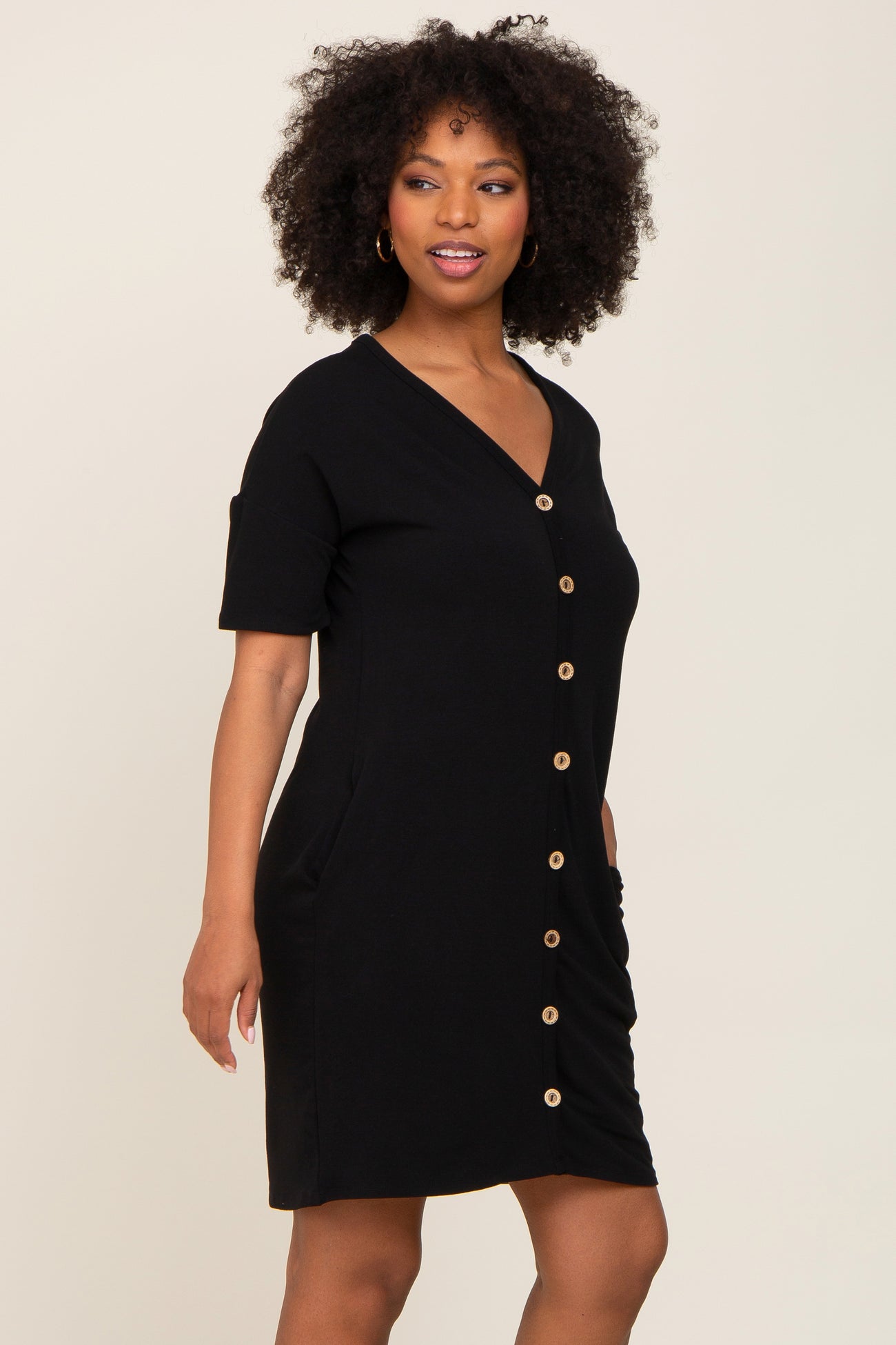 Woman with curly hair wearing a black short sleeve button down dress with gold buttons
