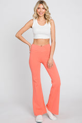 woman wearing white ribbed crop top and coral high waisted flare leggings with crossover waistband