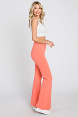 woman wearing white crop top and coral flare leggings standing against white background