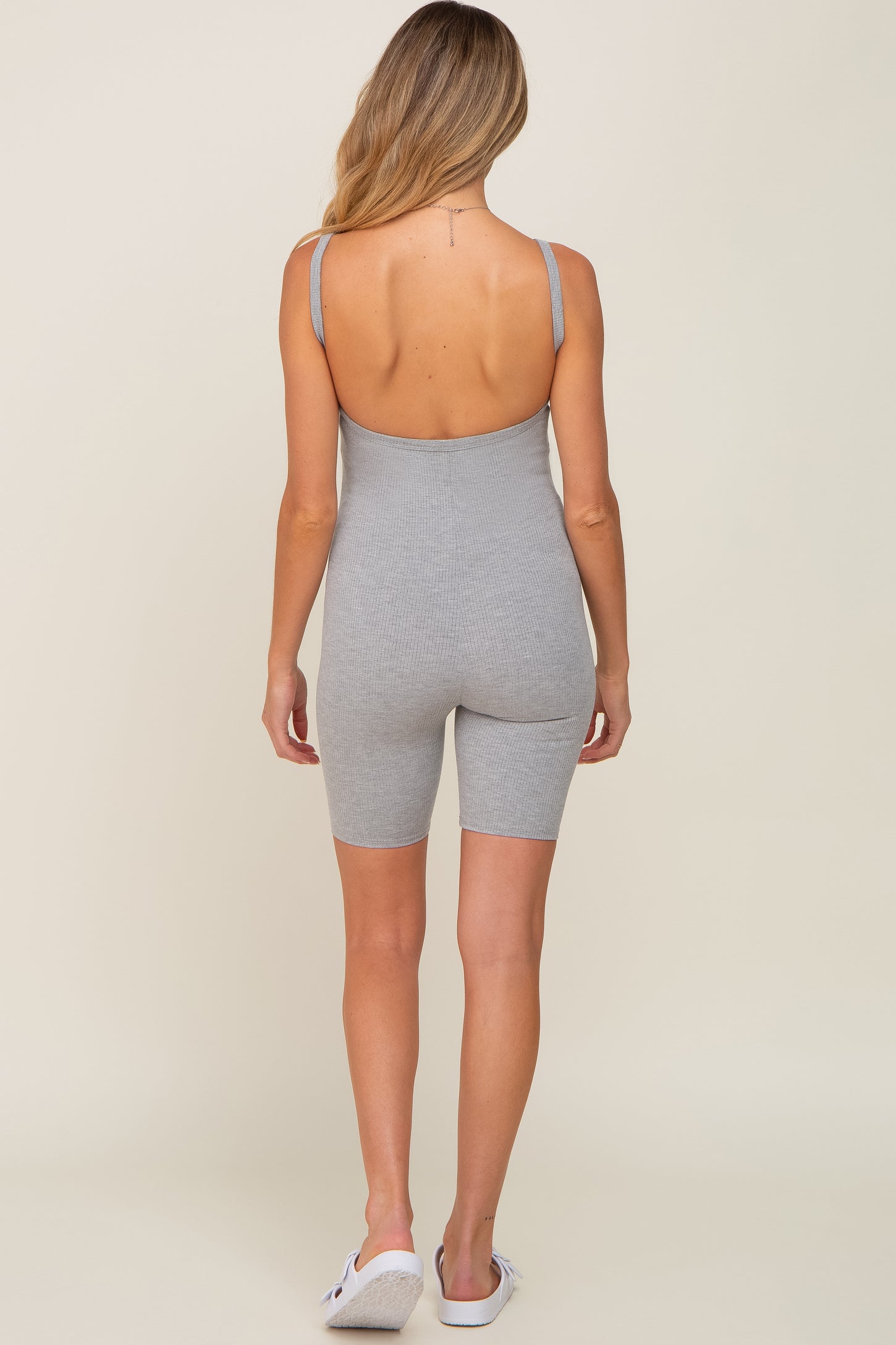 Back view of a woman wearing a grey ribbed sleeveless romper with a scoop back and biker short length