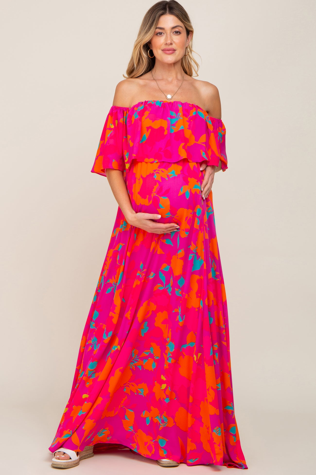 pregnant woman in pink floral off-the-shoulder maternity maxi dress holding her baby bump