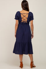 Back view of a woman wearing a navy blue midi dress with a lace-up back and ruffled hem