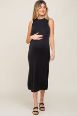Pregnant woman wearing a sleeveless black midi maternity dress and black sandals
