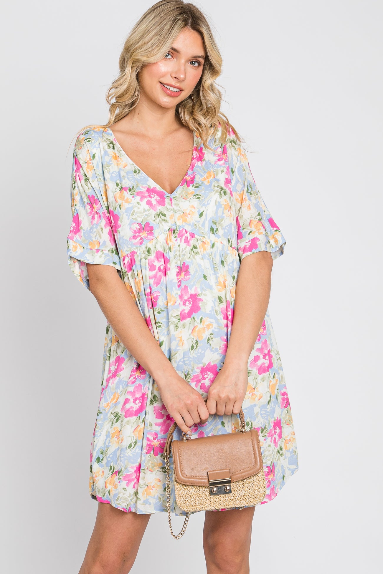 woman wearing a short sleeve floral print v-neck mini dress and holding a tan straw handbag