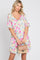 woman wearing a short sleeve floral print v-neck mini dress and holding a tan straw handbag