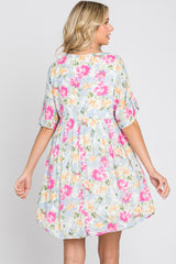 Back view of a woman wearing a short-sleeved floral babydoll dress with pink and yellow flowers on a light blue background