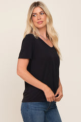 blonde woman wearing a black v-neck t-shirt and blue jeans against a neutral background