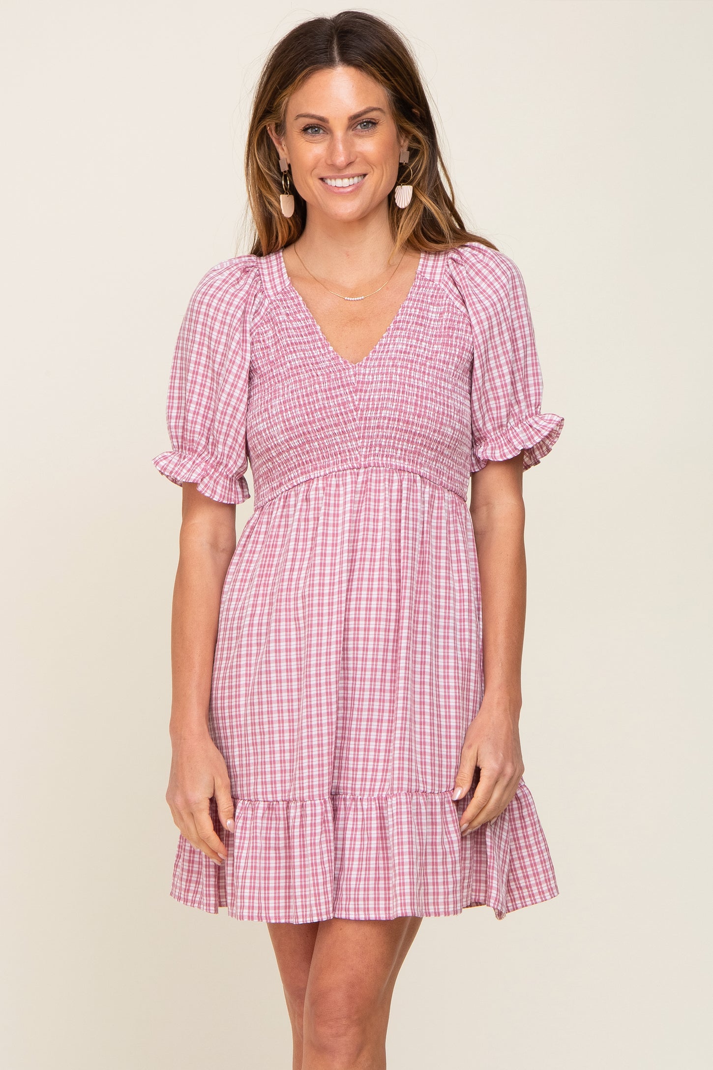 woman wearing a pink and white gingham smocked mini dress with puff sleeves and a ruffled hem