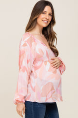 Smiling pregnant woman wearing a pink floral maternity blouse and blue jeans holding her baby bump