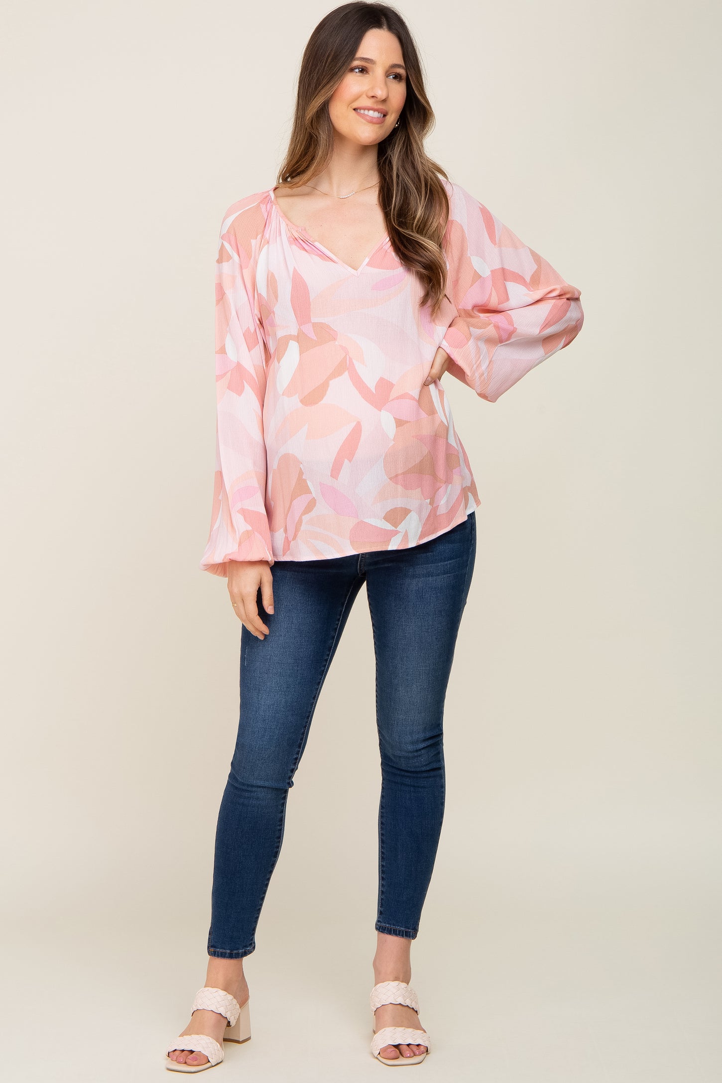 pregnant woman wearing a pink floral long sleeve maternity blouse and blue skinny jeans