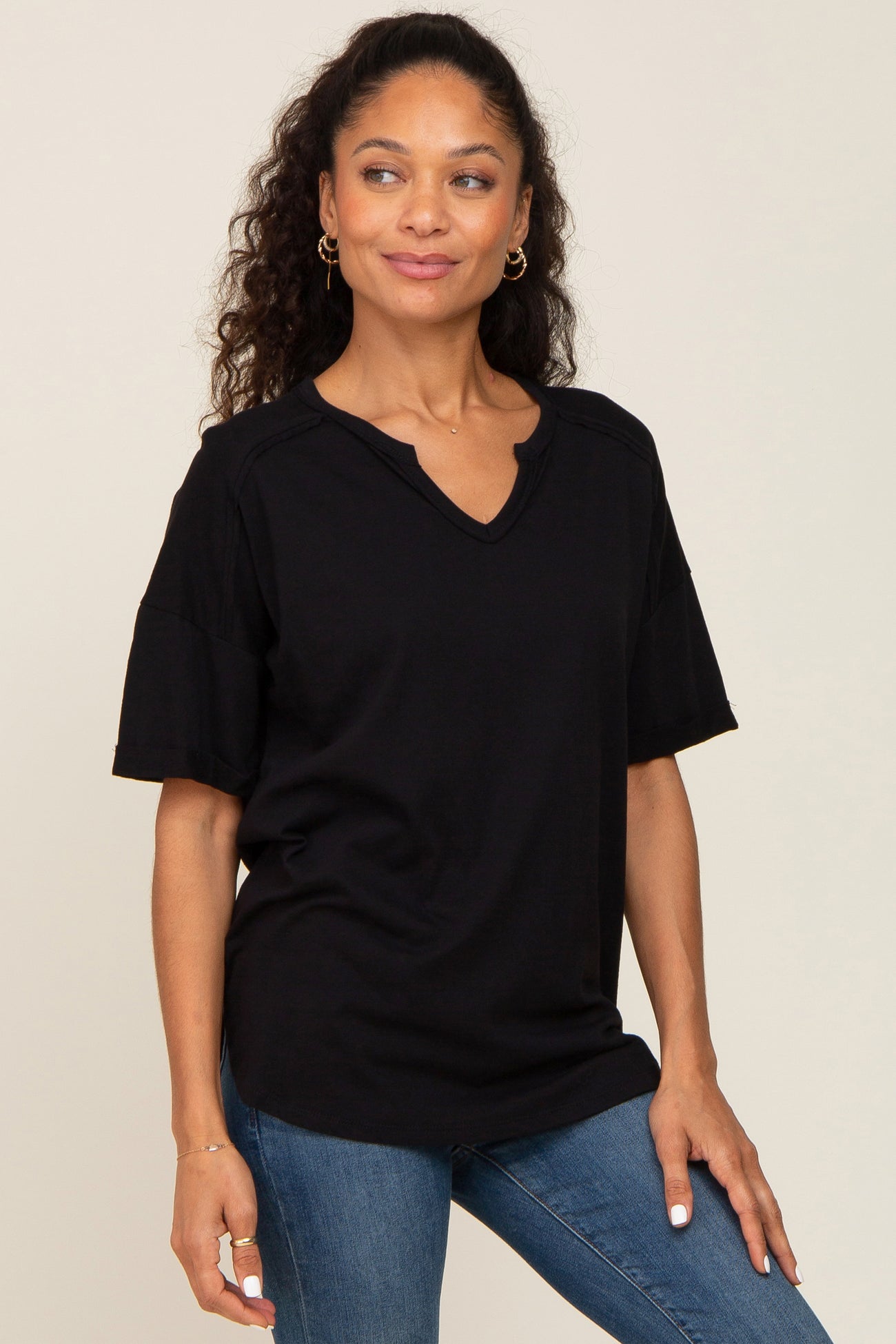 woman wearing a black short sleeve v-neck t-shirt and blue jeans against a neutral background