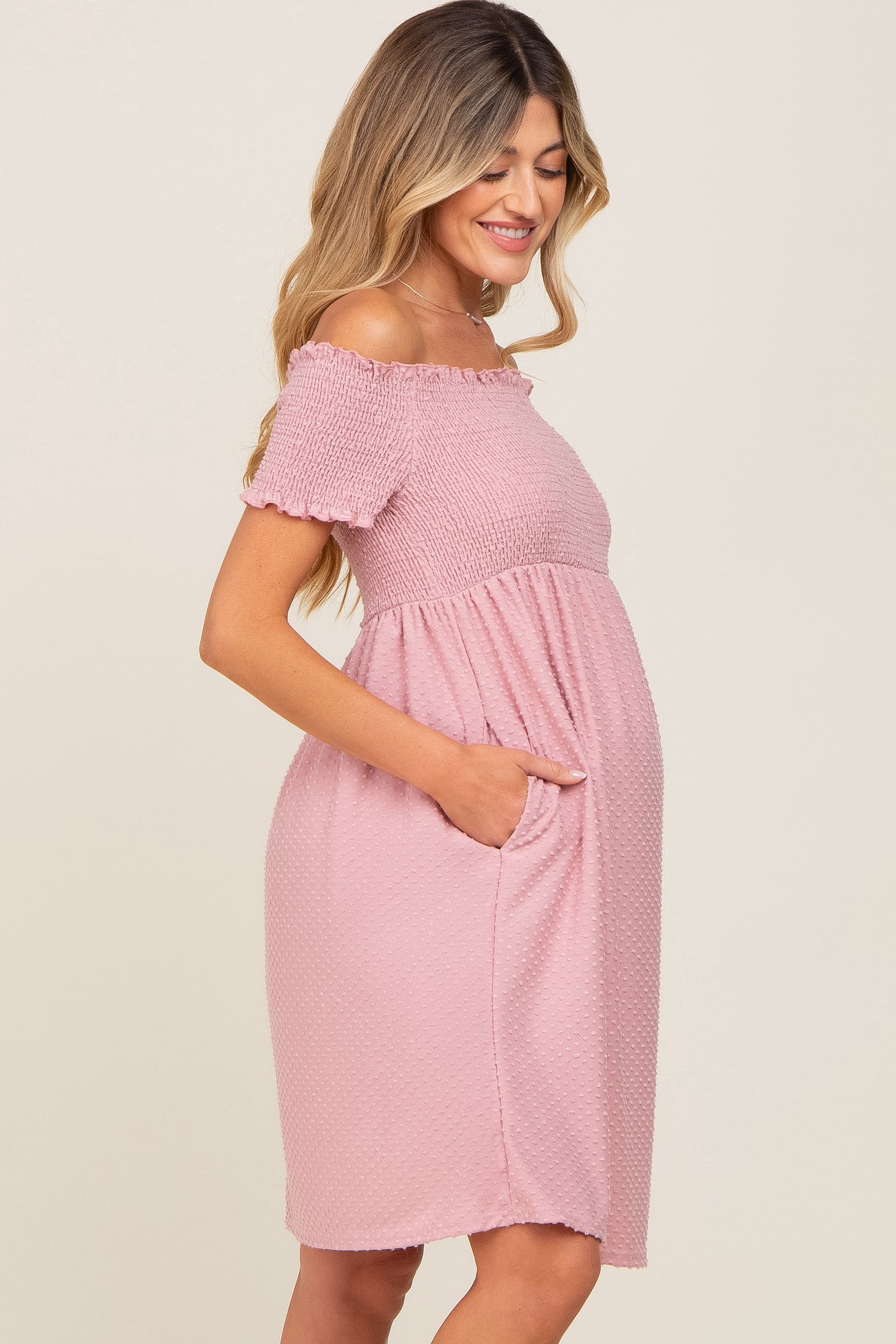 smiling pregnant woman wearing a pink off-the-shoulder smocked maternity dress with pockets