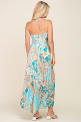 Back view of a woman wearing a teal and peach floral halter maxi dress with white block heel sandals