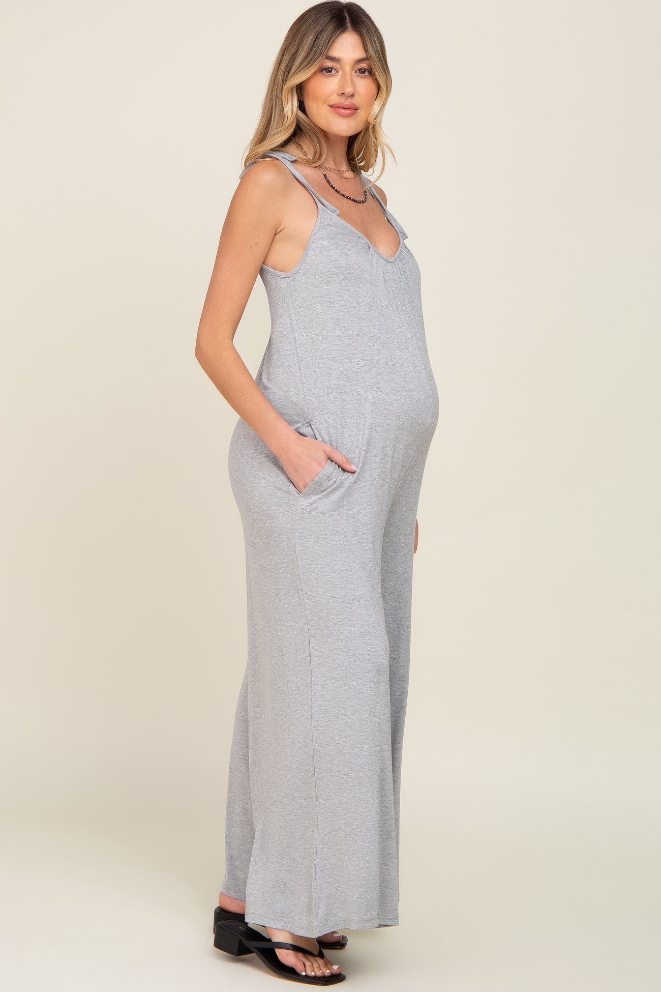 Pregnant woman wearing a grey sleeveless maternity jumpsuit with wide legs and side pockets