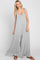 Woman wearing a grey sleeveless wide-leg jumpsuit with tie straps and brown sandals against a white background