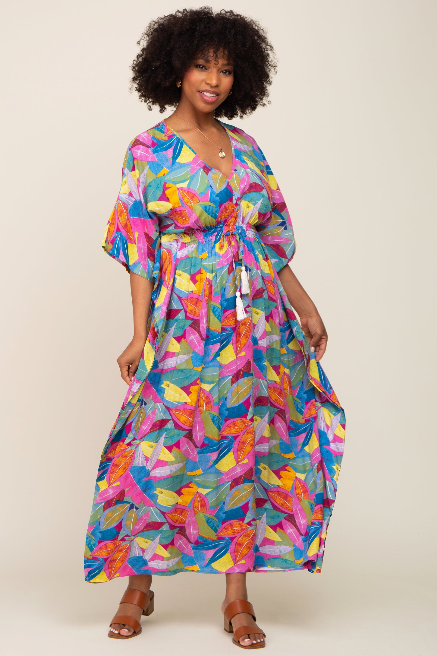woman wearing a colorful maxi dress with a leaf print and a cinched waist, standing against a light background