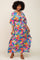 woman wearing a colorful maxi dress with a leaf print and a cinched waist, standing against a light background