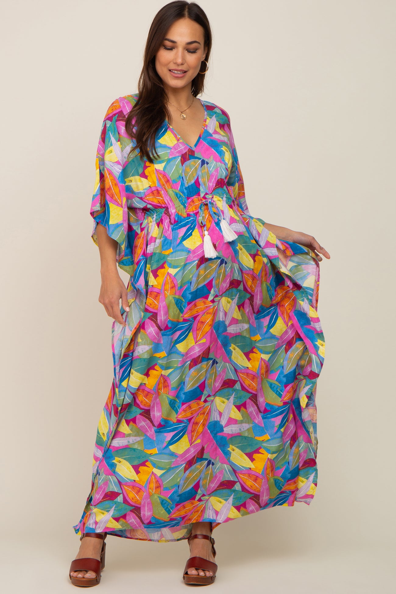 woman wearing a colorful floral print maternity maxi dress with a tie waist and flowing sleeves, displaying her baby bump